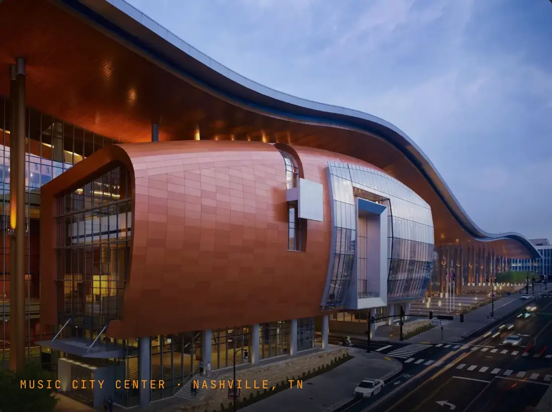 Music City Center exterior at dusk — Nashville, Tennessee convention center hosting Bitcoin 2027, featuring its distinctive curved copper facade and glass curtain walls along Rep. John Lewis Way S